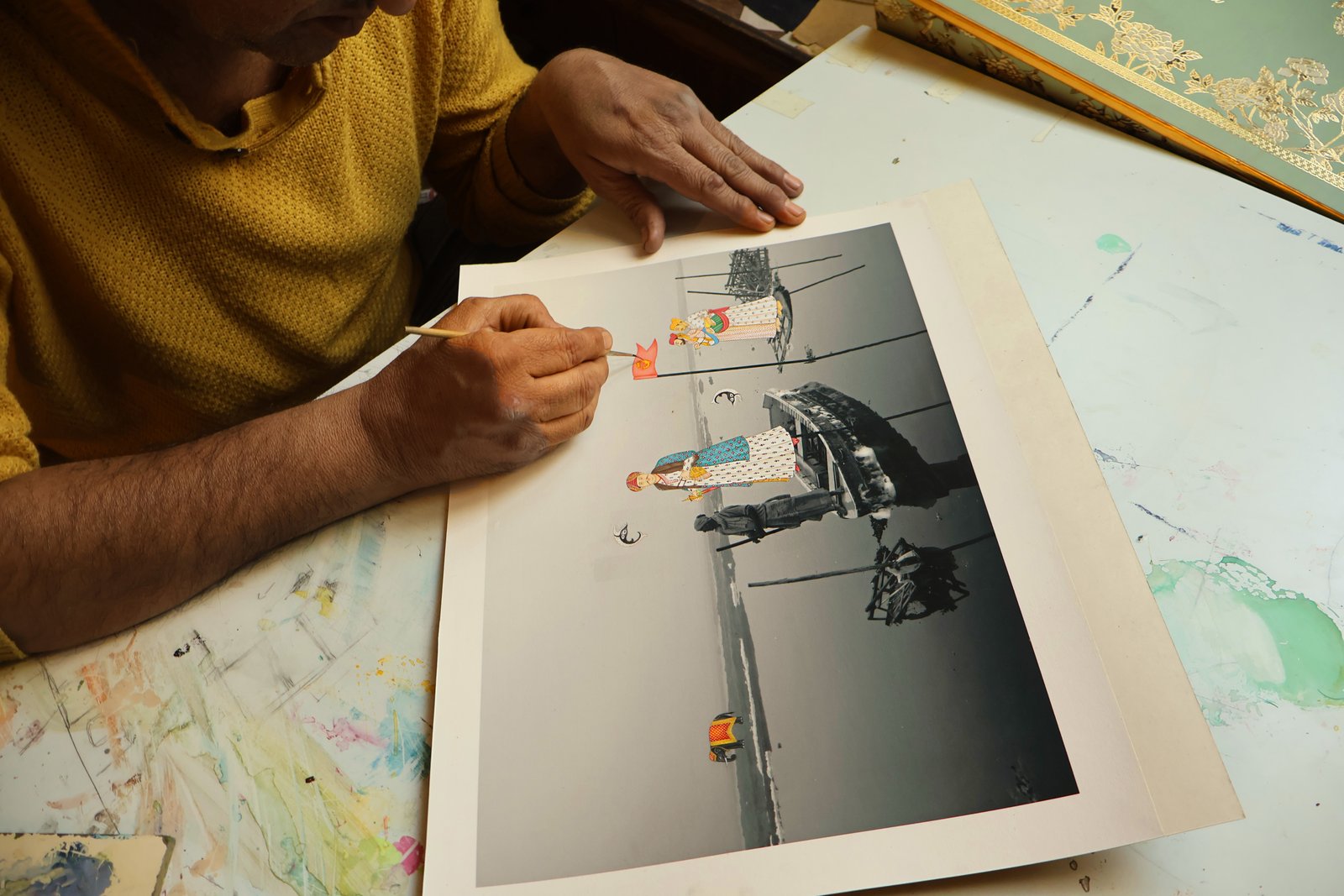 A miniature artist hand-painting figures onto a photographic print on rice paper